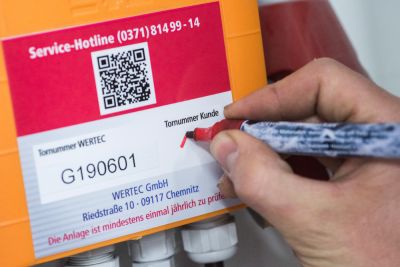 ein Wertec-Mitarbeiter trägt auf einem Wartungslabel die Tornummer nach Prüfung ein